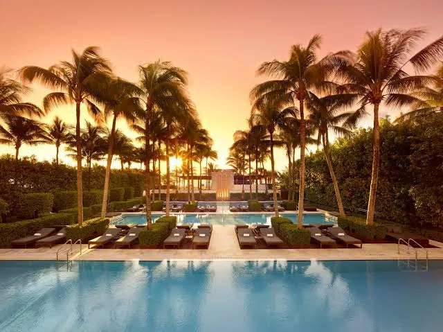 Outdoor pool surrounded by lounge chairs, palm trees, and lush hedges at sunset; serene water and fresh air invite relaxation—offering a peaceful setting to support gut health through stress reduction and mindful downtime.